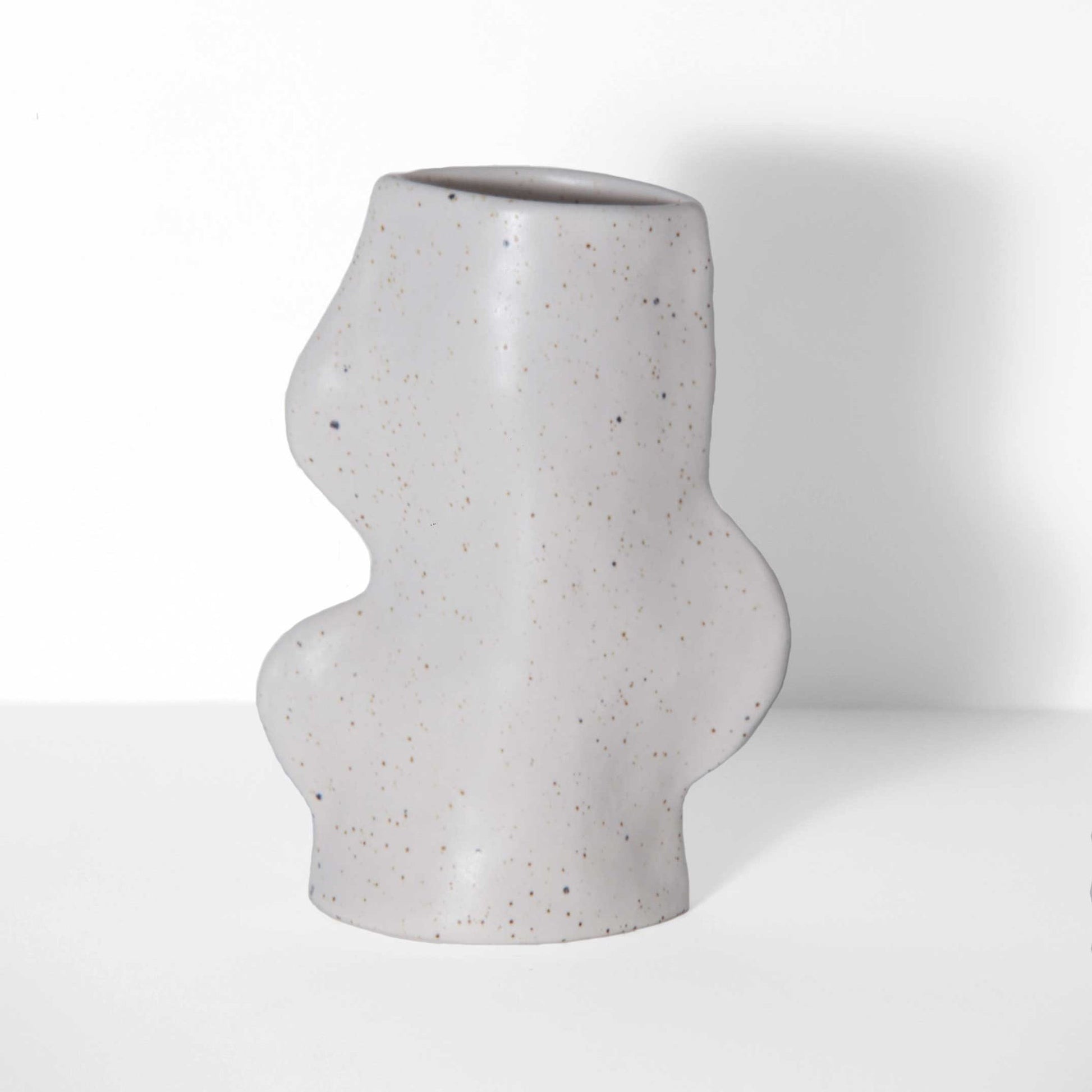 playful white ceramic vase with smooth flowing lines on a bright yellow table