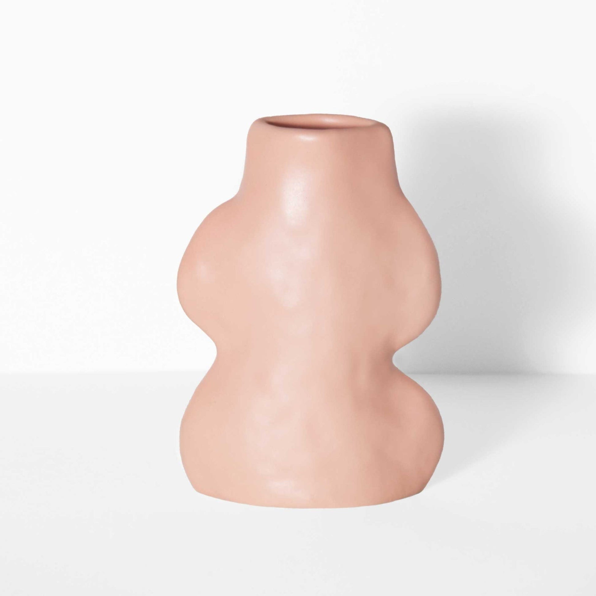 playful pink ceramic vase with flowing lines on a bright windowsill, casting a fun shadow