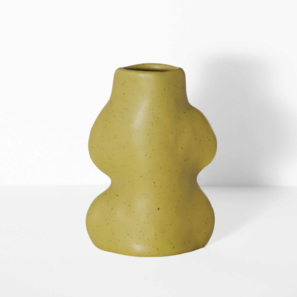 small pistachio ceramic vase on a tabletop holding a single dried flower stem