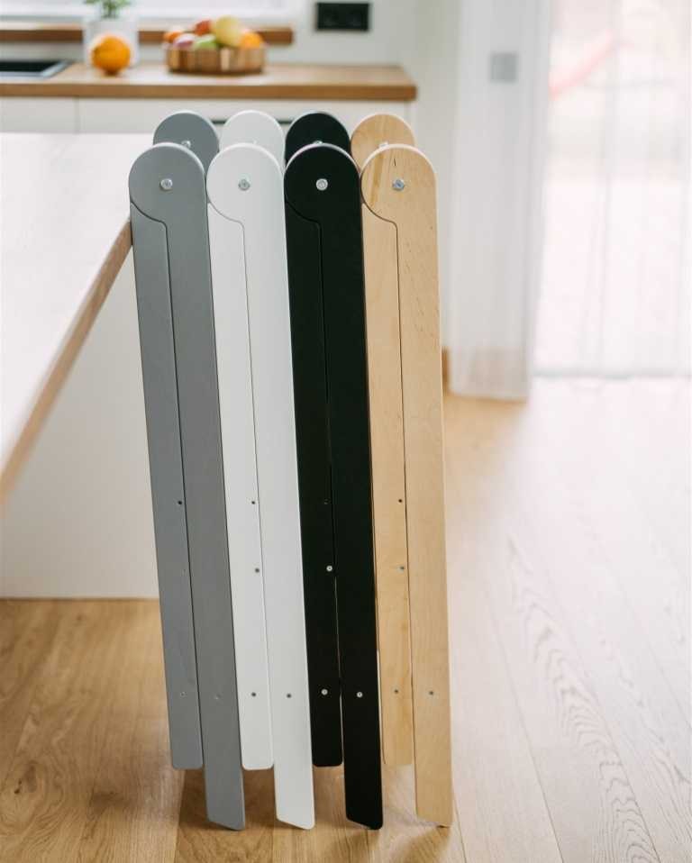 a playful toddler in a sunlit kitchen, proudly using the foldable helper tower to bake cookies