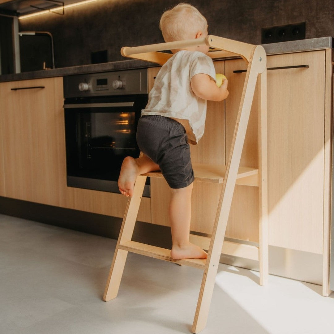 foldable kitchen helper tower in a bright, sunlit kitchen with a child safely baking
