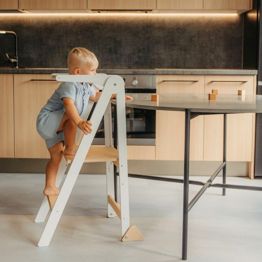a foldable kitchen helper tower in a sunlit room, showcasing its sleek finnish birch profile and safety rail