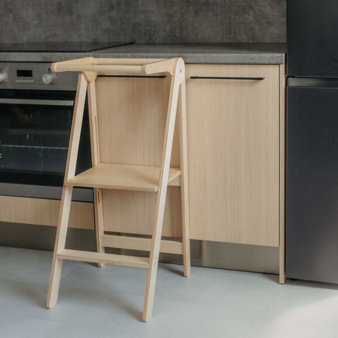 foldable kitchen helper tower shown in warm morning light, folded flat against a sunlit wall