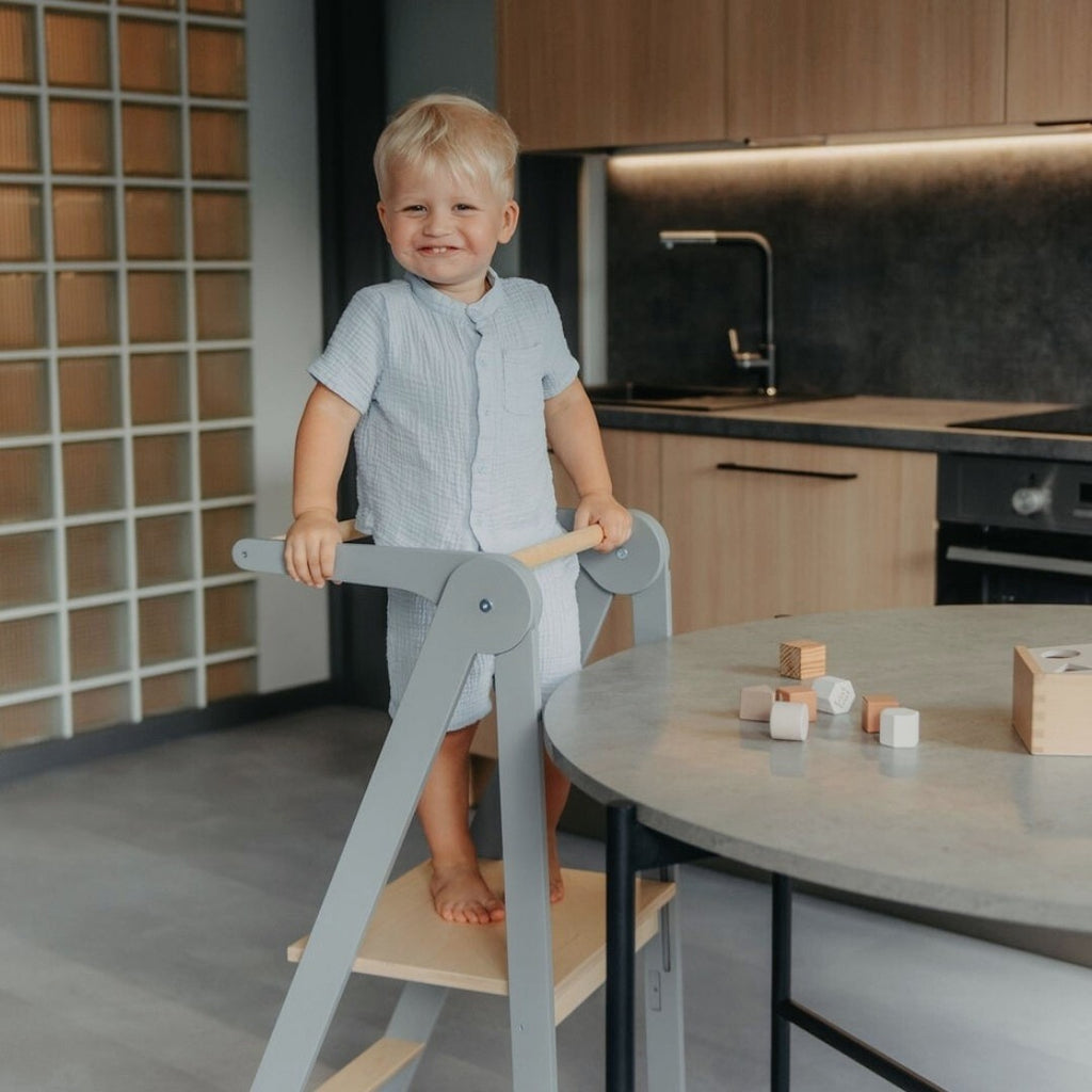 a foldable kitchen helper tower with safety rail in a softly lit nursery setting