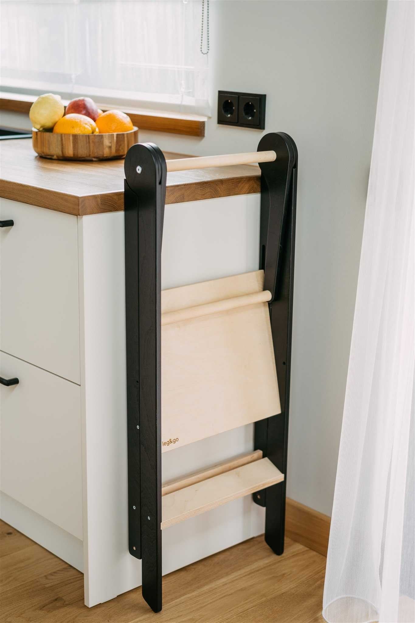 a foldable kitchen helper tower with a safety rail in a soft, warm-lit nursery setting