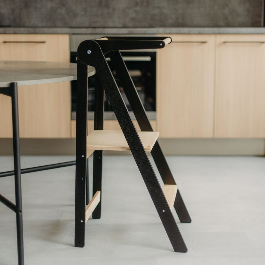 a soft-lit kitchen helper tower with a safety rail folded compactly against a wall