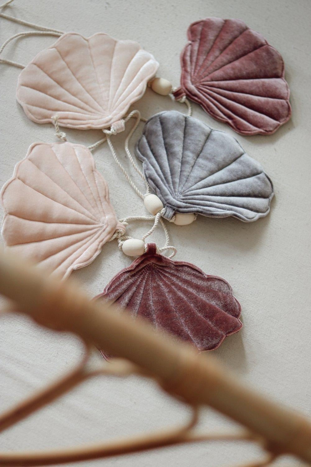 cosmic pearl shell garland draped elegantly over a rustic wooden shelf, marsala and apricot shells catching warm light