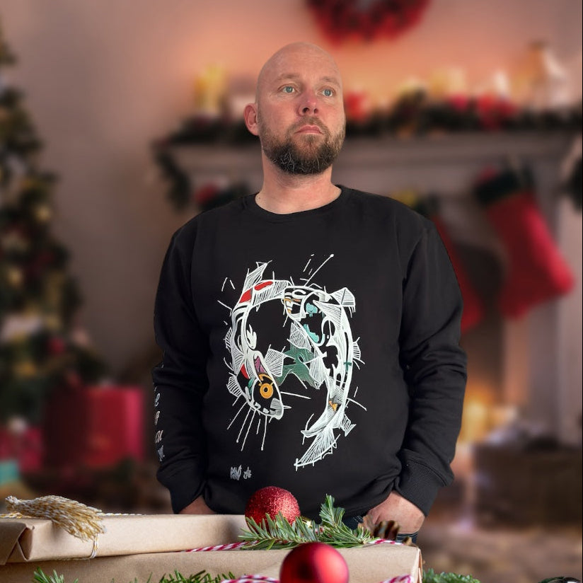 Man in a black sweater with a decorative design, standing behind wrapped gifts and Christmas decorations. sostter.pro