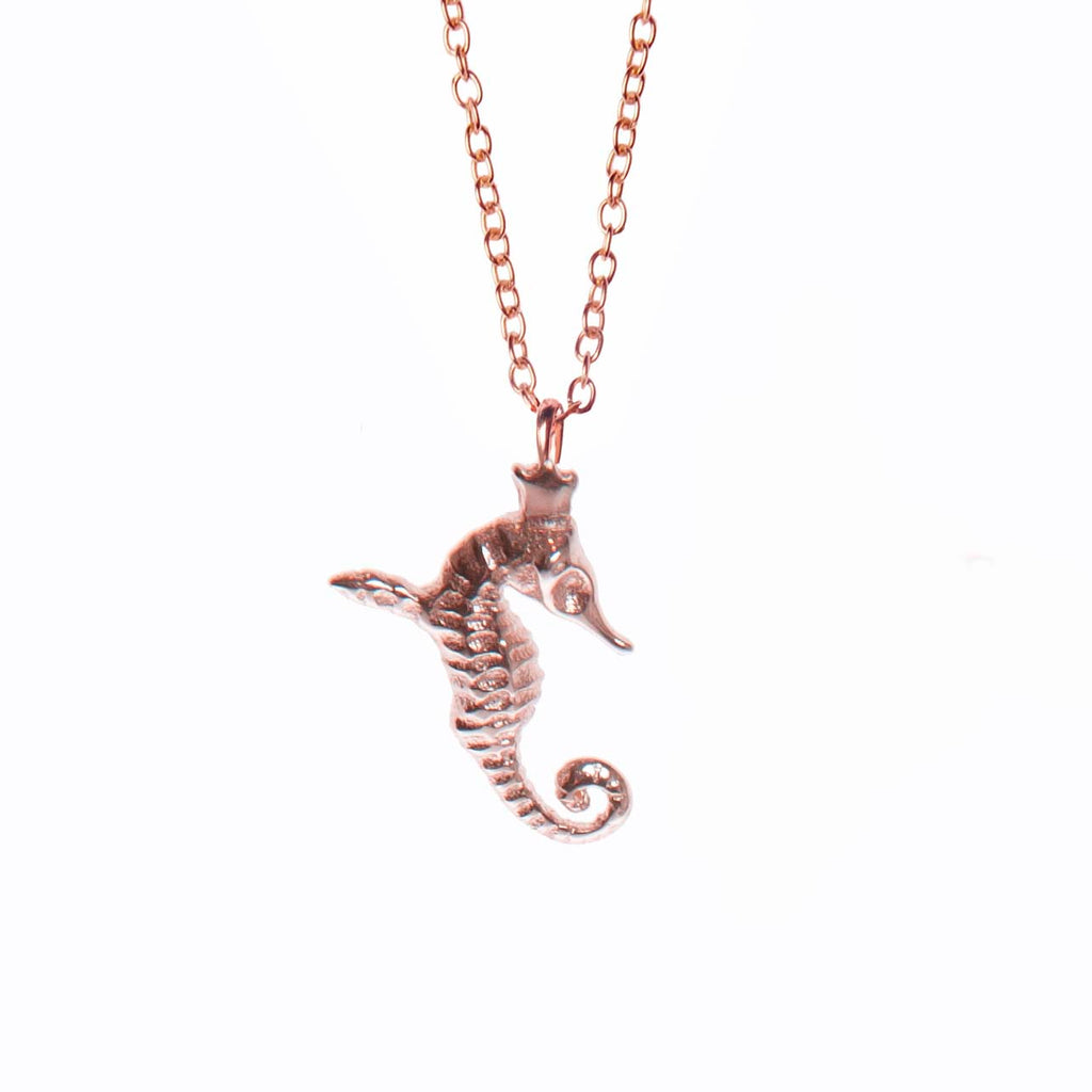 bold close-up of a rose gold hippocamp pendant with sharp details against a dark background