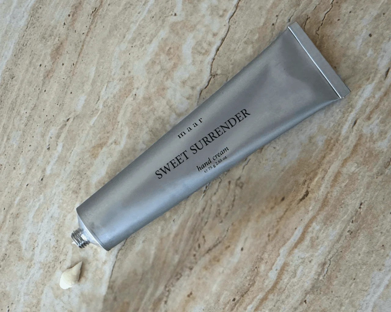 a soft-focus close-up of sweet surrender hand cream being gently squeezed from its tube