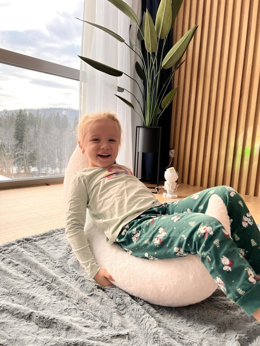 a soft crescent moon pillow nestled in a cozy nursery corner, its plush faux fur glowing gently in the warm lamplight