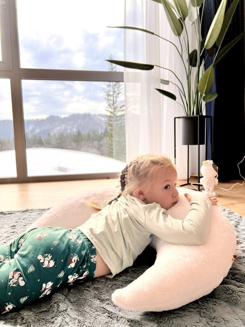 a toddler giggling while hugging a giant faux fur moon pillow in a sunlit nursery