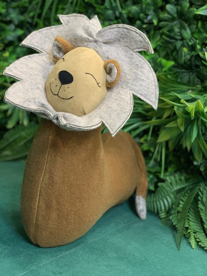a playful lion cuddle pillow in warm lamplight, its soft brown fur and felt details inviting a hug