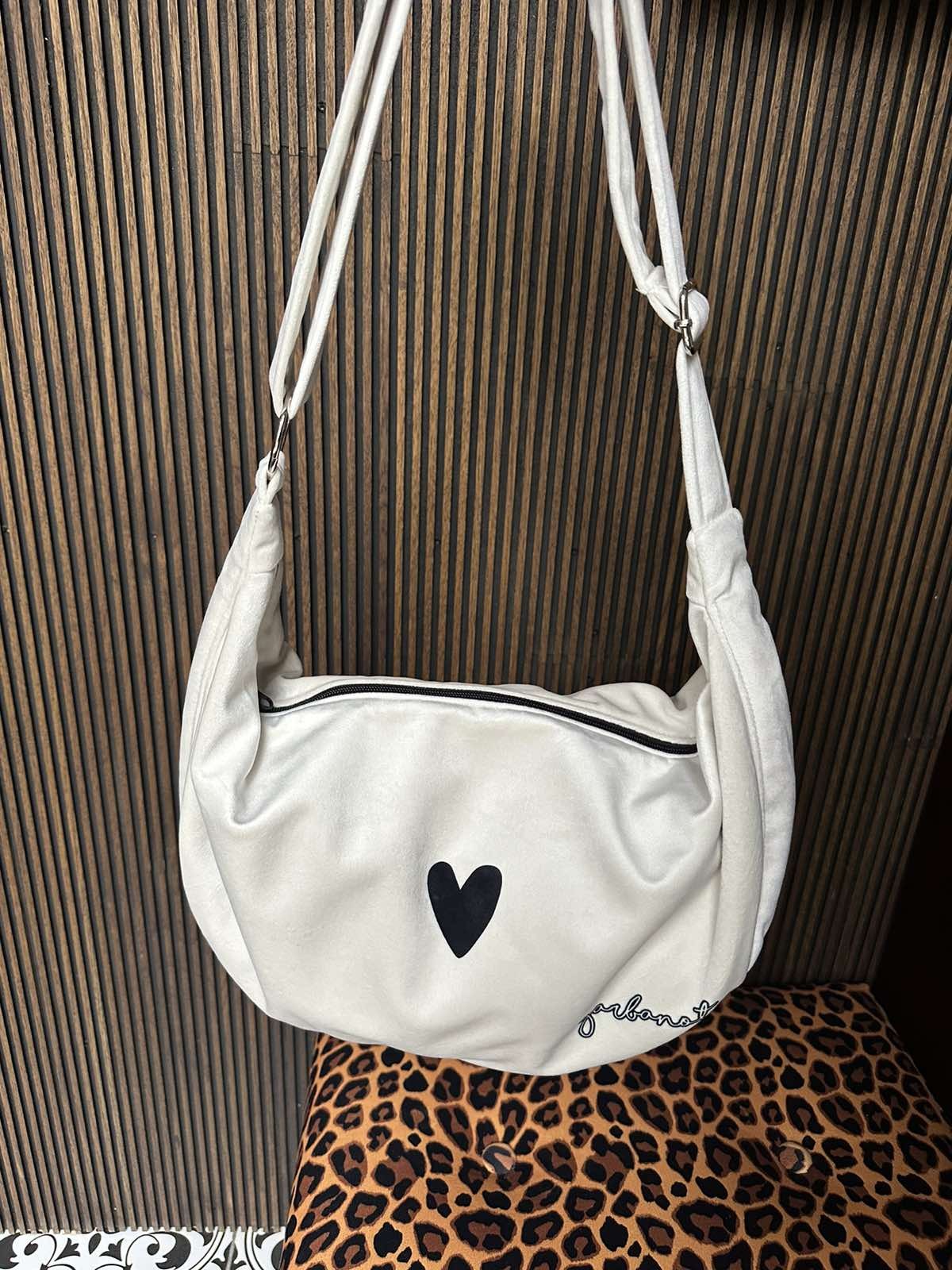 white velour hobo bag with heart charm on a sunny park bench, strap extended