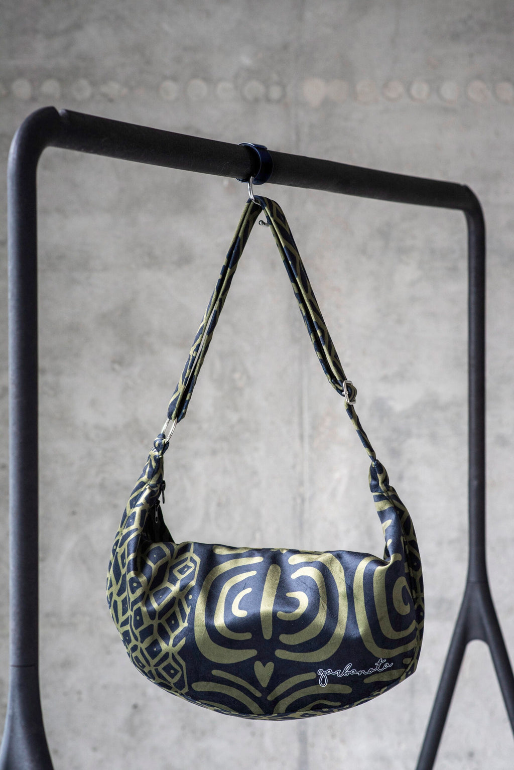 a woman's functional khaki velour hobo bag with an adjustable strap, shown on a wooden table