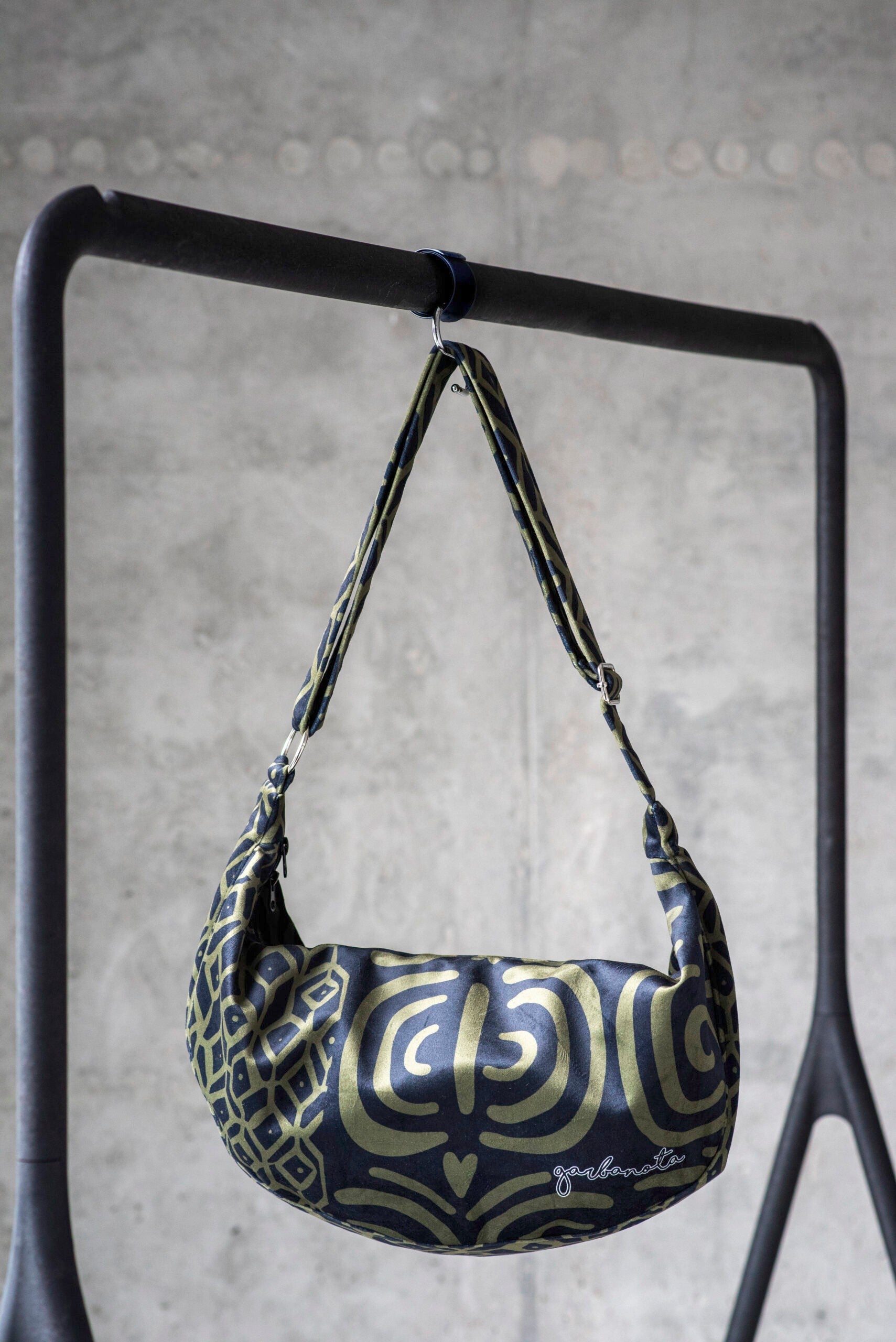 a woman's functional khaki velour hobo bag with an adjustable strap, shown on a wooden table