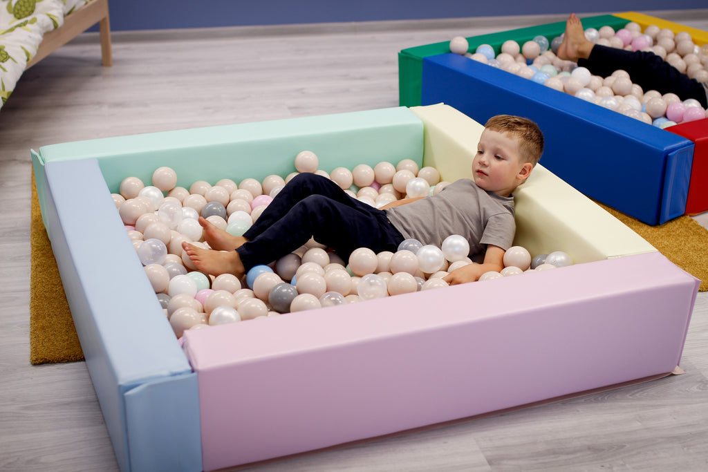 confident toddler playing in a light pastel soft play ball pit