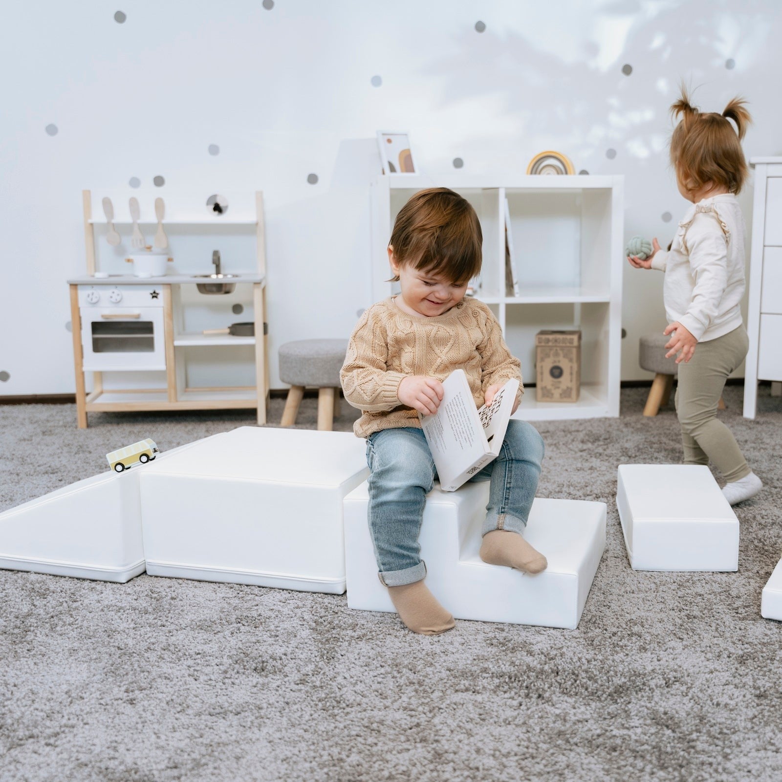 a child's hand reaching for the soft white corner climber foam block in a sunlit playroom