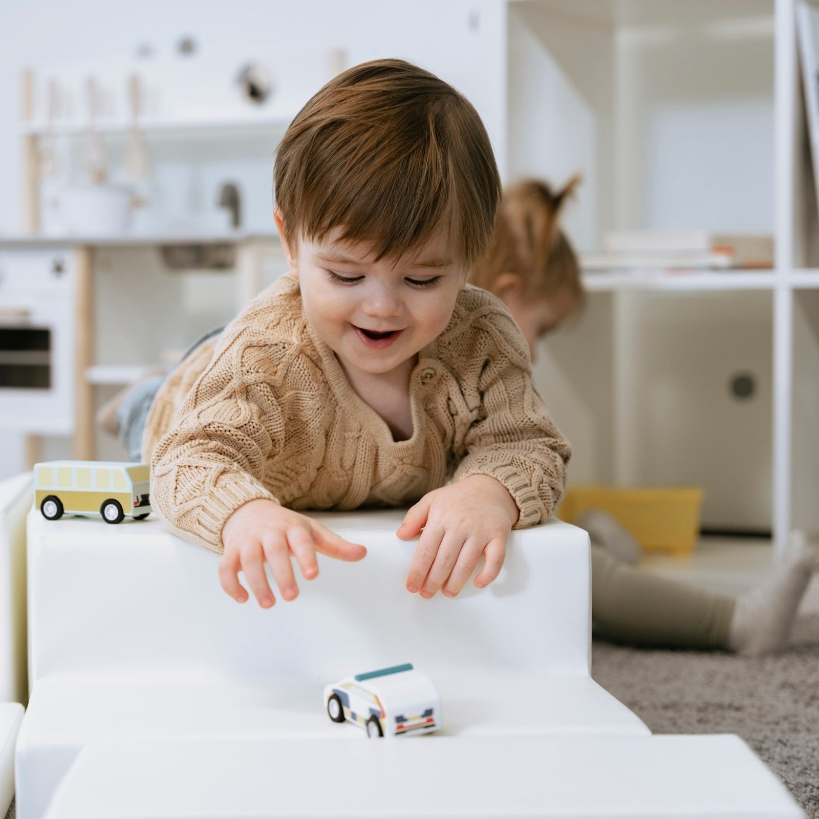 toddler climbing on a white foam corner climber in a soft morning-lit playroom