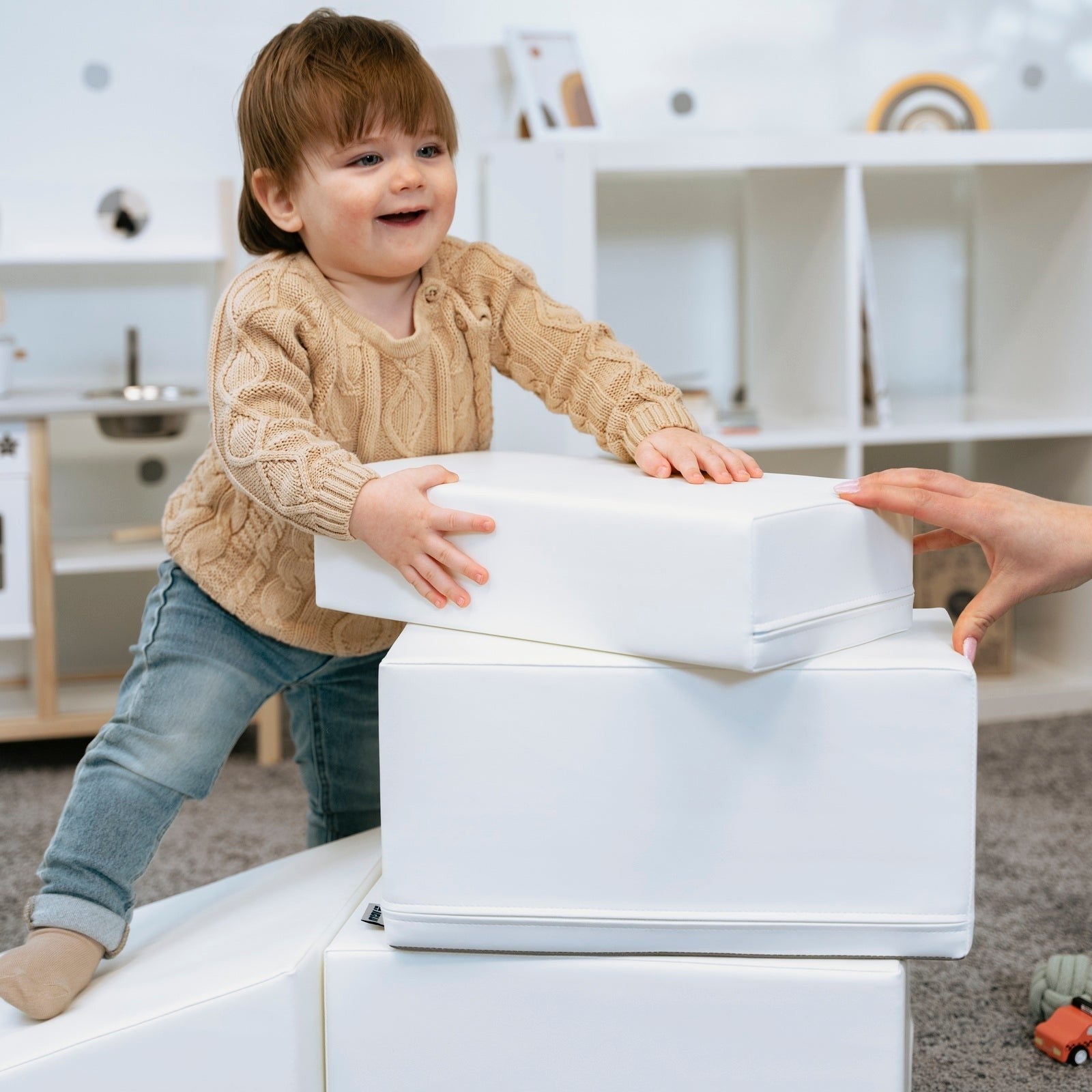 a toddler in soft morning light carefully balances on a white foam corner climber block