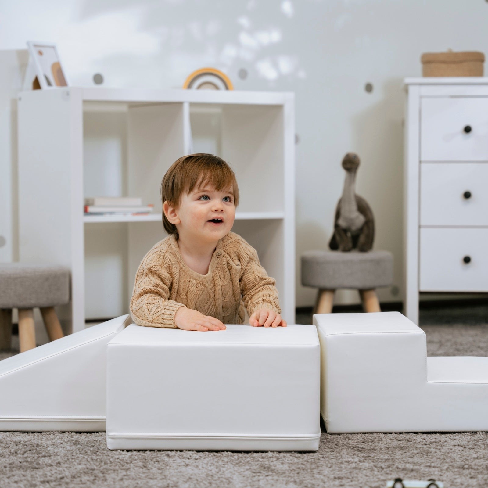 a child's hand reaching for a soft white foam climber block in a sunlit playroom