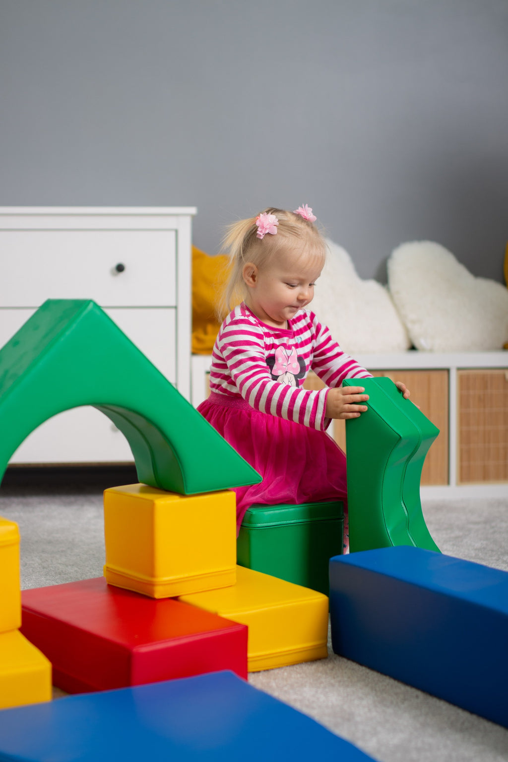 a child's hand stacking a vibrant iglu foam block in a sunlit playroom