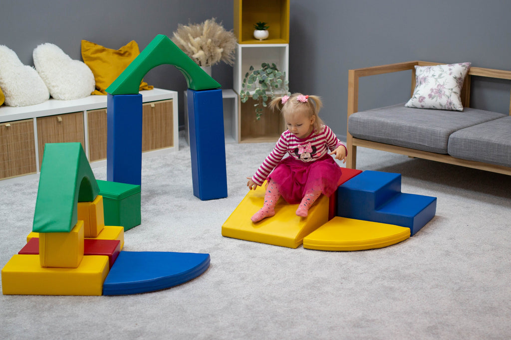 a child's hand stacking a vibrant iglu foam block in a sunlit playroom