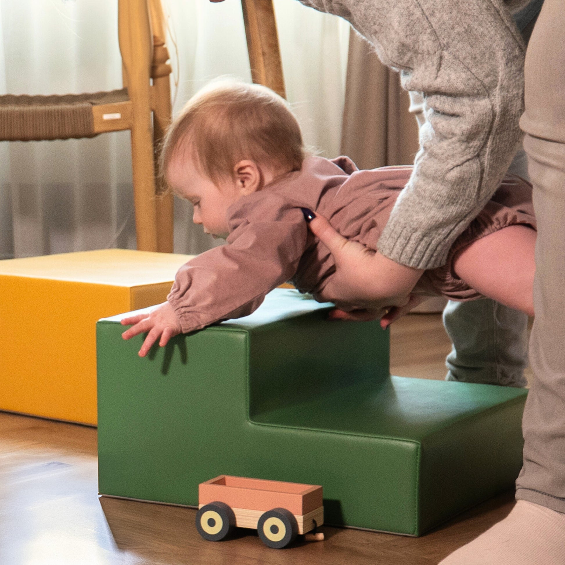 a toddler's hand reaching for a pastel turquoise foam block in a sunlit playroom