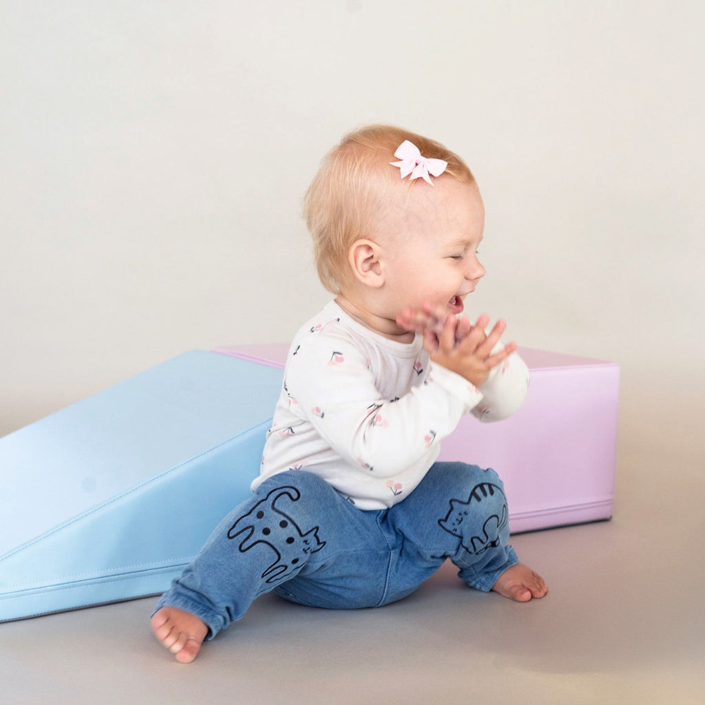 a toddler carefully balancing on a soft pastel foam block climber in warm morning light