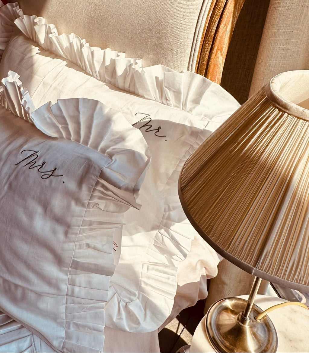 White pillow with 'Mrs.' embroidery on a chair next to a lamp on sostter.pro