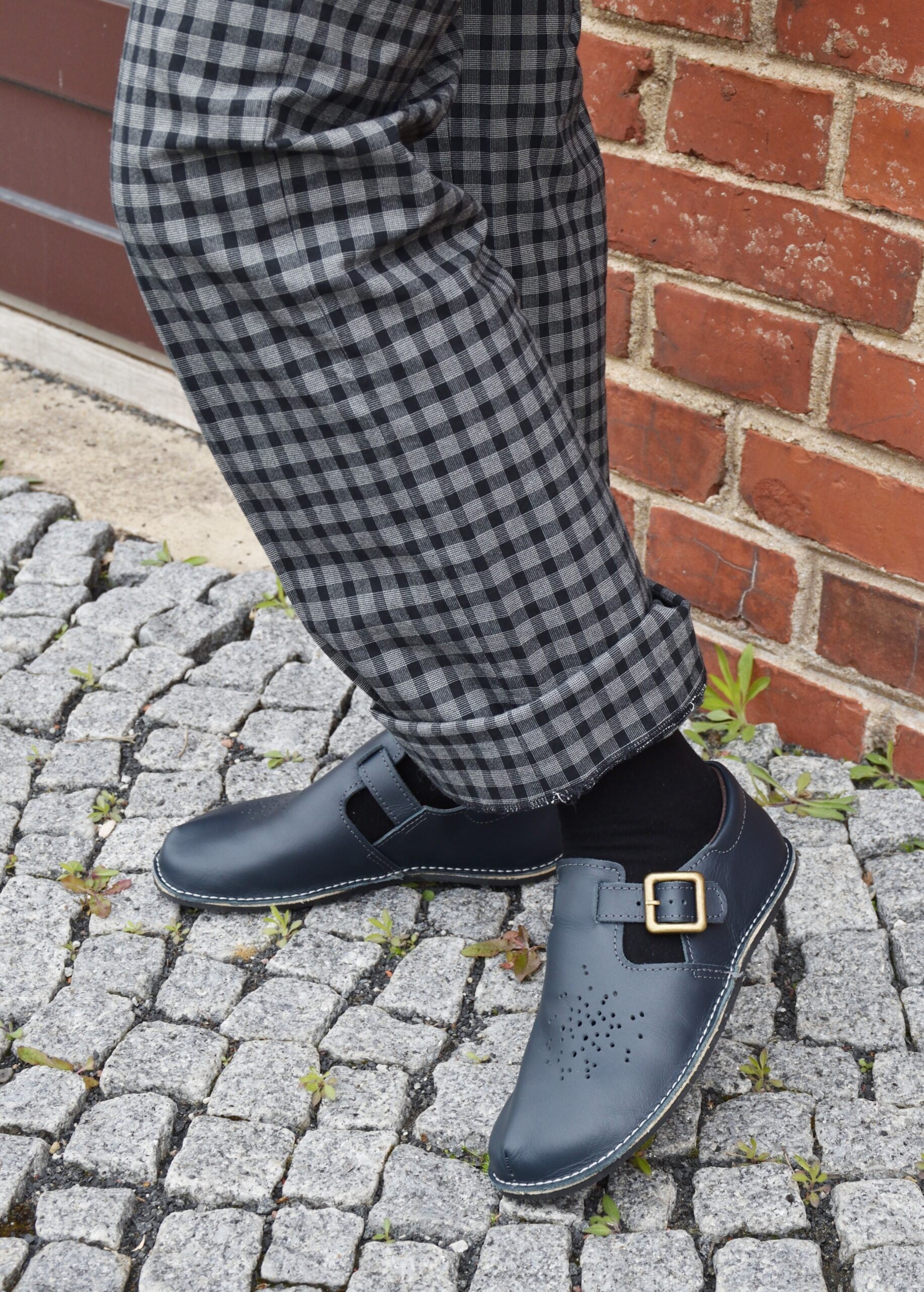 playful side view of dark blue kuuda shoes on a sunny day, showing the flexible sole and adjustable buckle