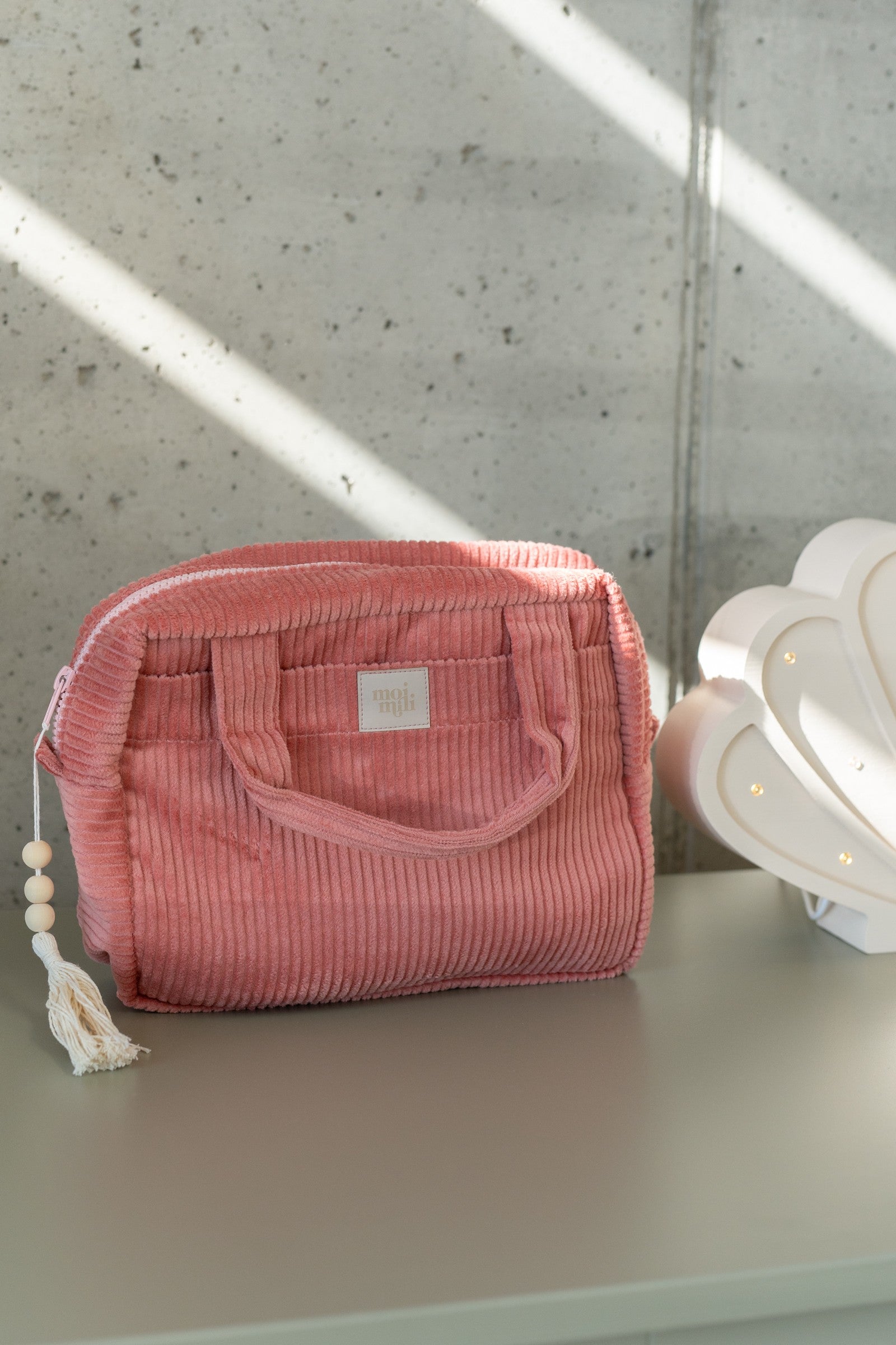 a playful coral makeup bag open on a sandy beach, showing its inner pockets and cotton texture
