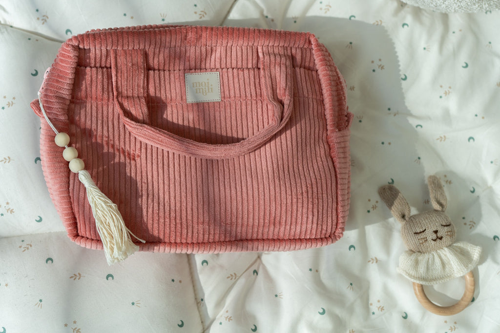 a coral cotton makeup bag on a sandy beach, open to show its inner waterproof lining and pockets