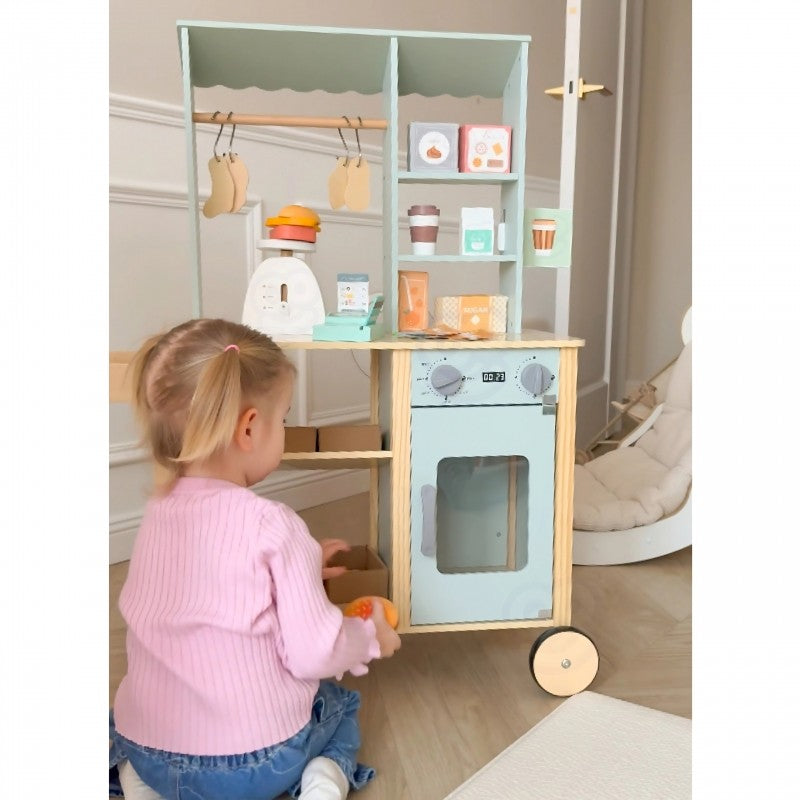 a child's hand using the green food truck's card reader to ring up a wooden apple
