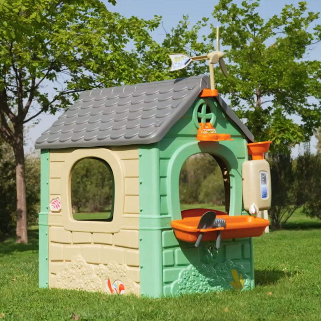 soft-lit recycled eco playhouse with blue and yellow bins, wind turbine, and cozy bird feeder in a sunlit garden