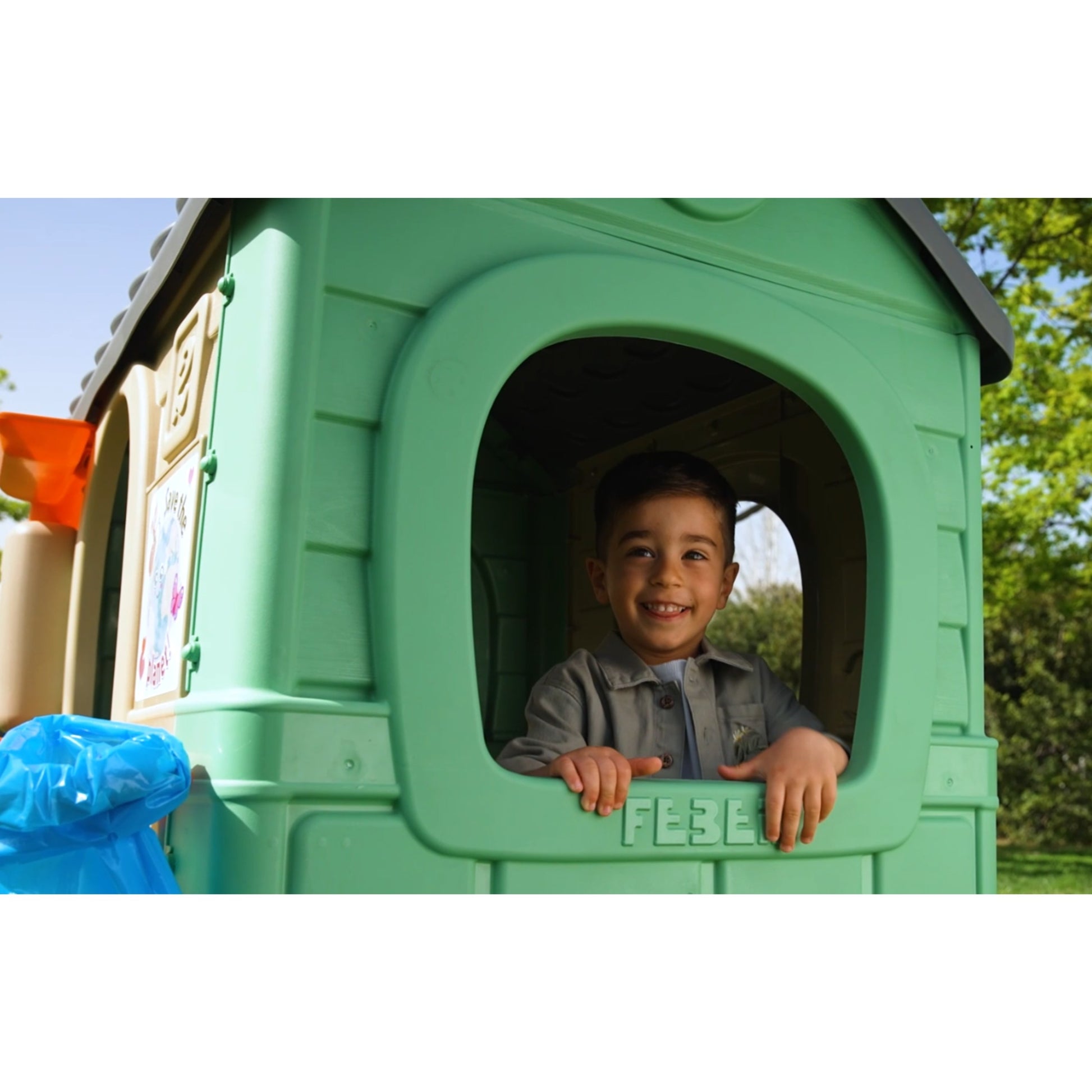 kids playing in a recycled eco playhouse with wind turbine and solar panels under golden sunset light