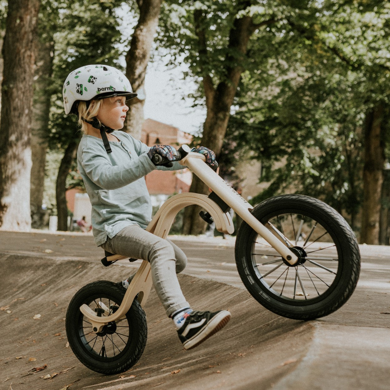 a toddler laughing on a wooden balance bike in a sunlit park