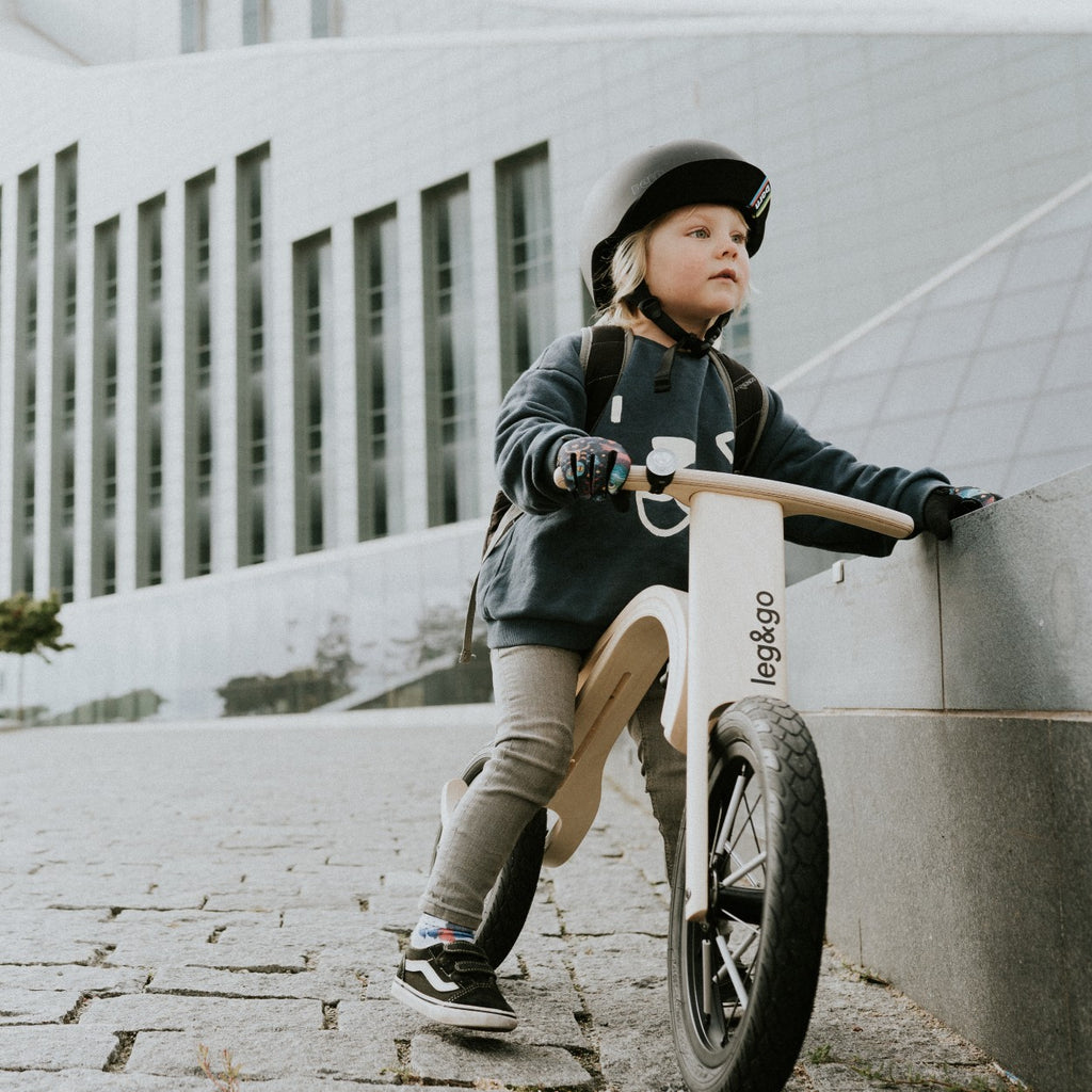 a close-up side view of the wooden balance bike, showing the adjustable seat height and inflatable tires on a neutral background