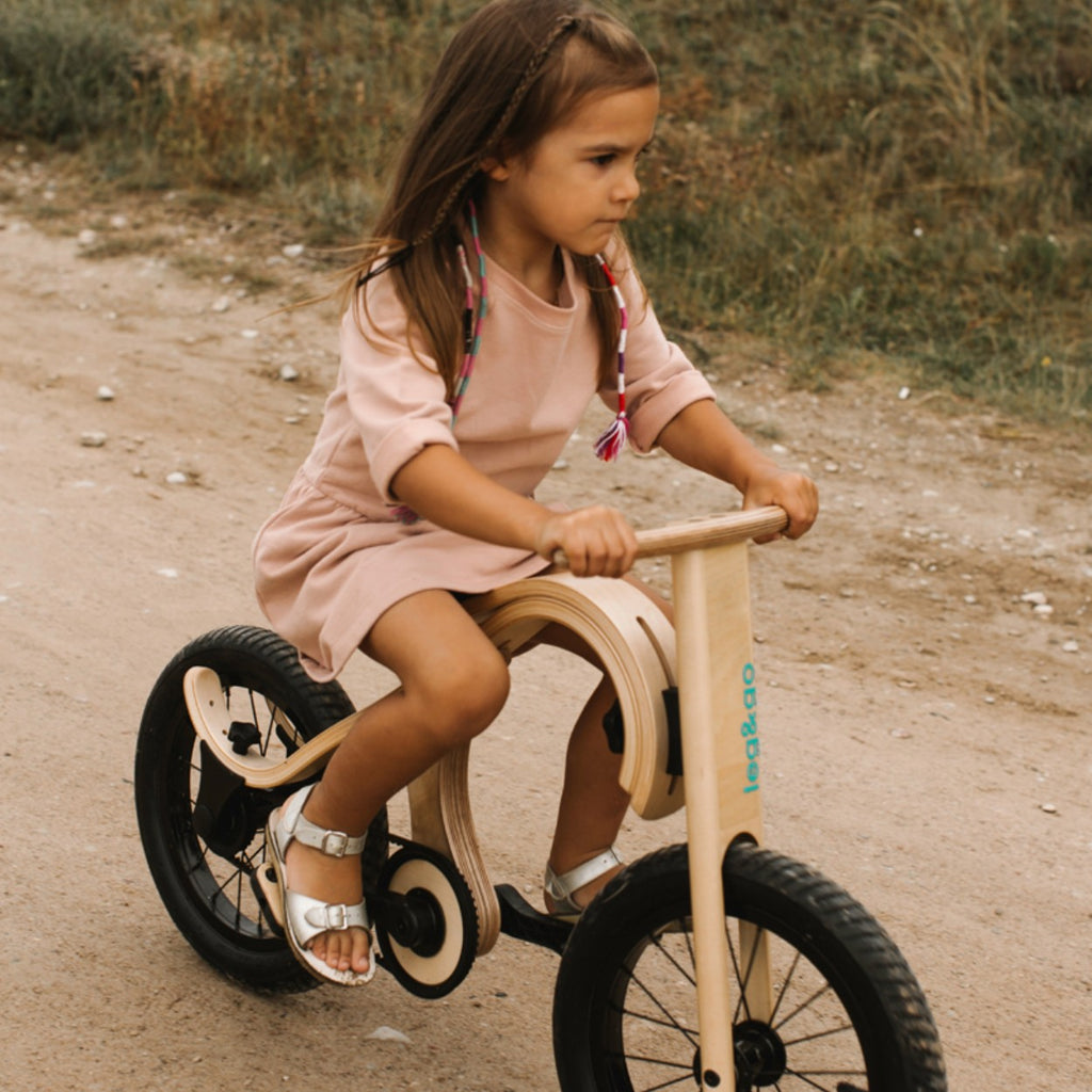 a child's hand gleefully spinning the pedal on a wooden balance bike conversion kit