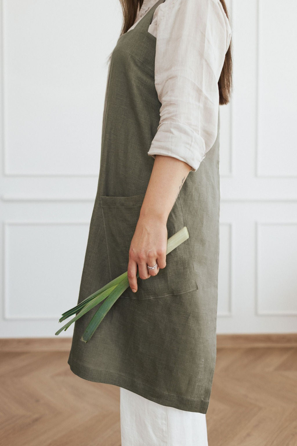 a playful woman in a linen apron laughing while cooking, showing off the stylish crossed back straps