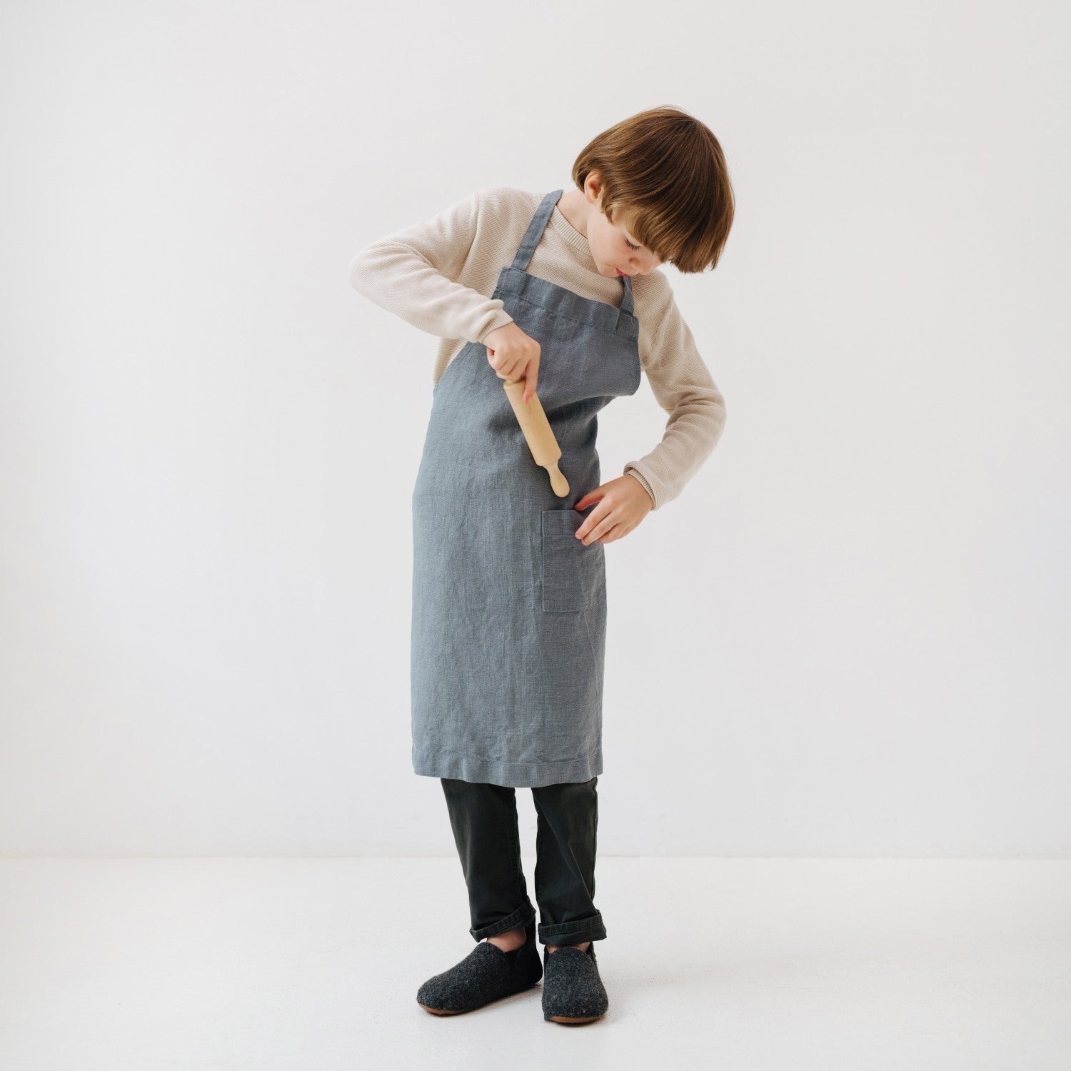 a child's soft blue fog linen apron with a front pocket, shown in comforting morning light