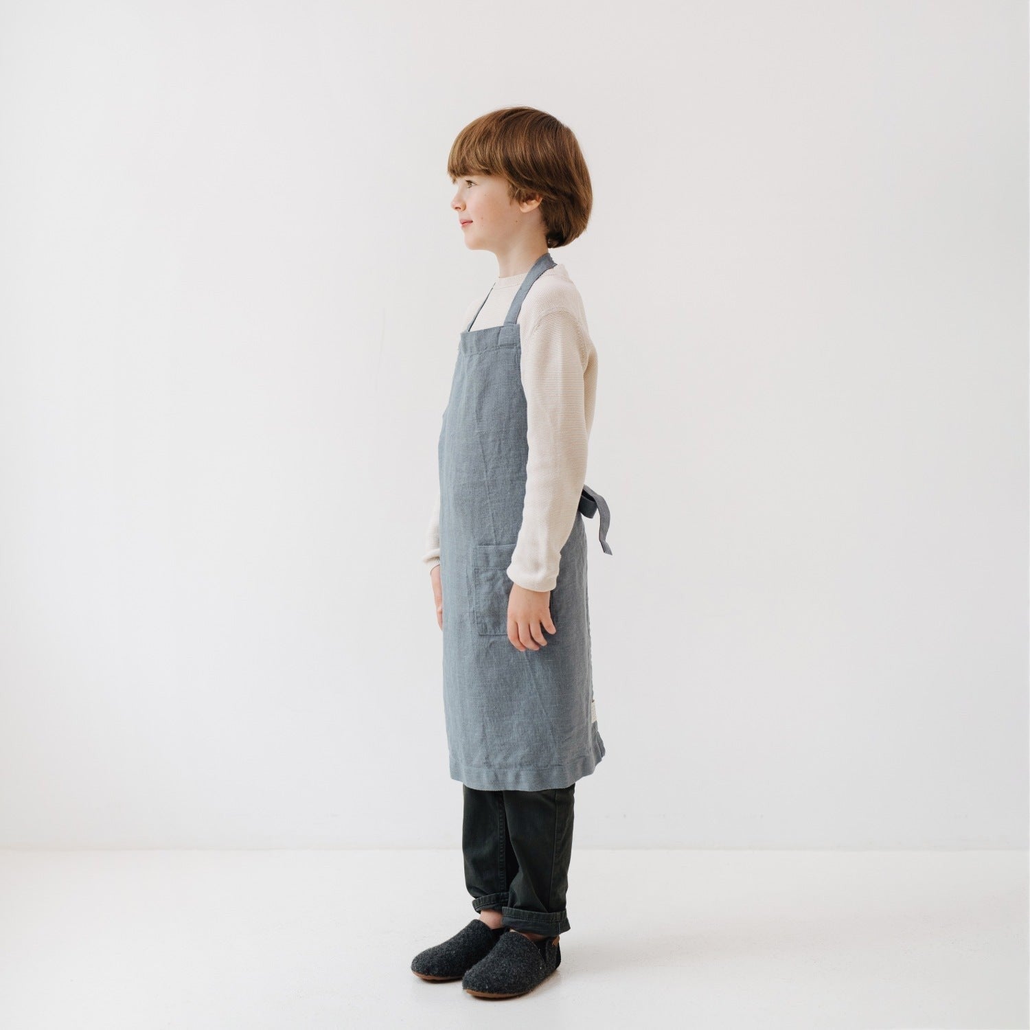 elegant blue fog linen kids apron with a front pocket, shown in soft morning light