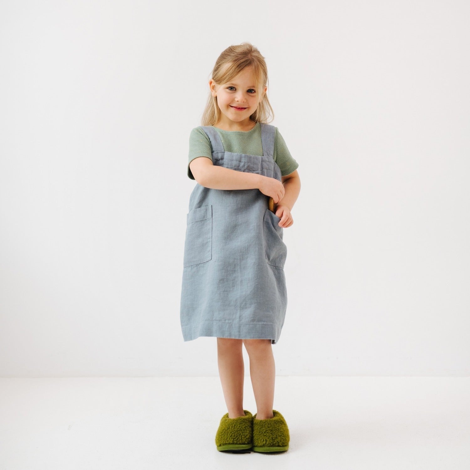 a child laughing, twirling to show off the blue fog linen pinafore apron with full pockets