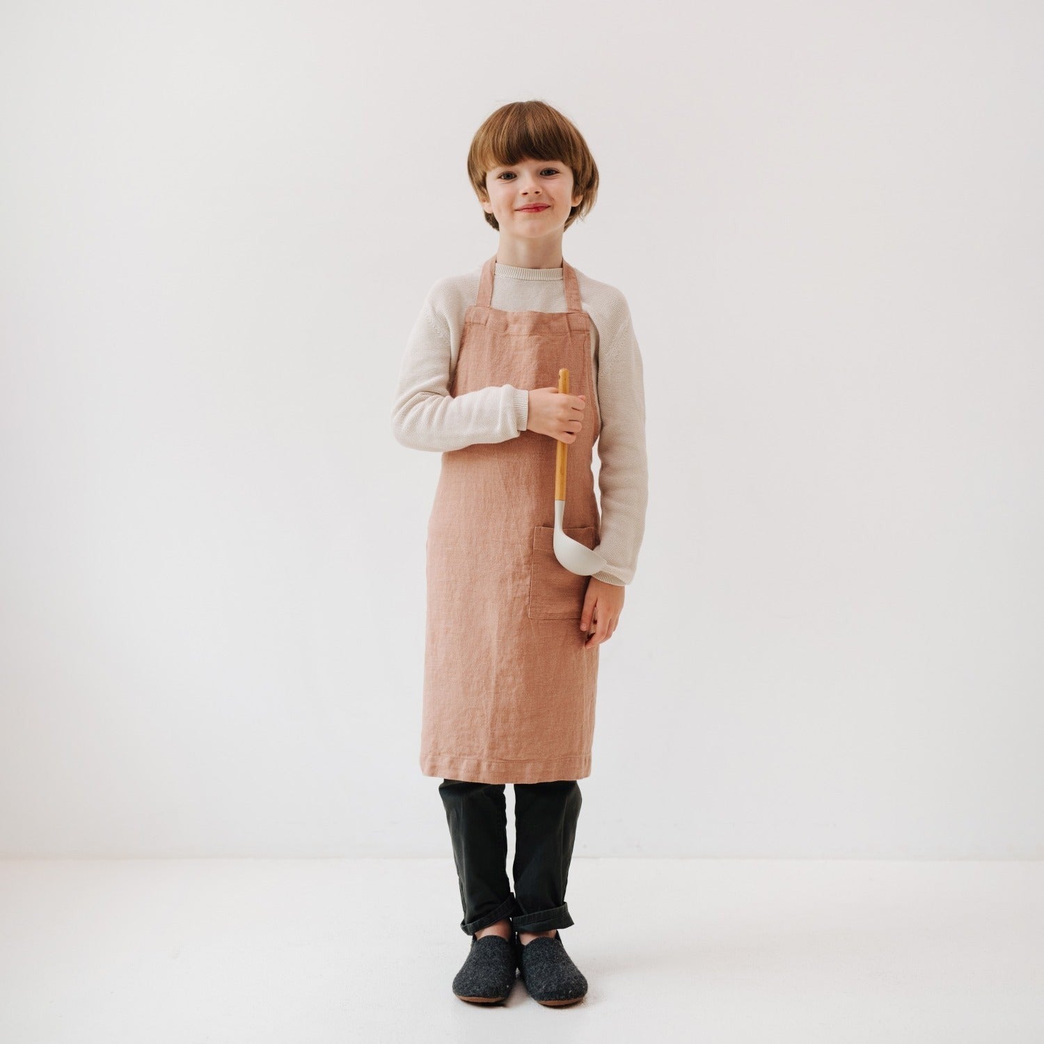 a child wearing a soft cafe creme linen apron, focused on baking with tools in the front pocket