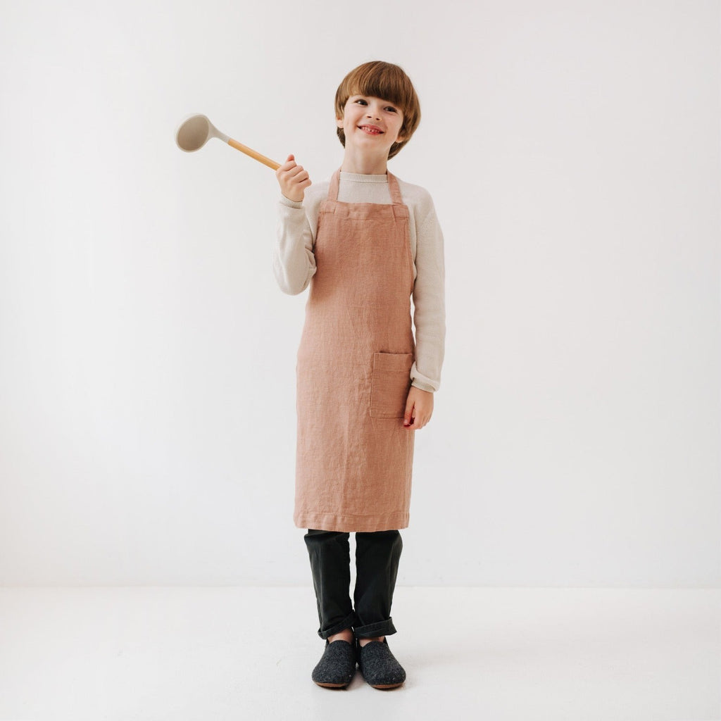 a child laughing in a linen apron, holding a whisk and ready for a fun baking adventure