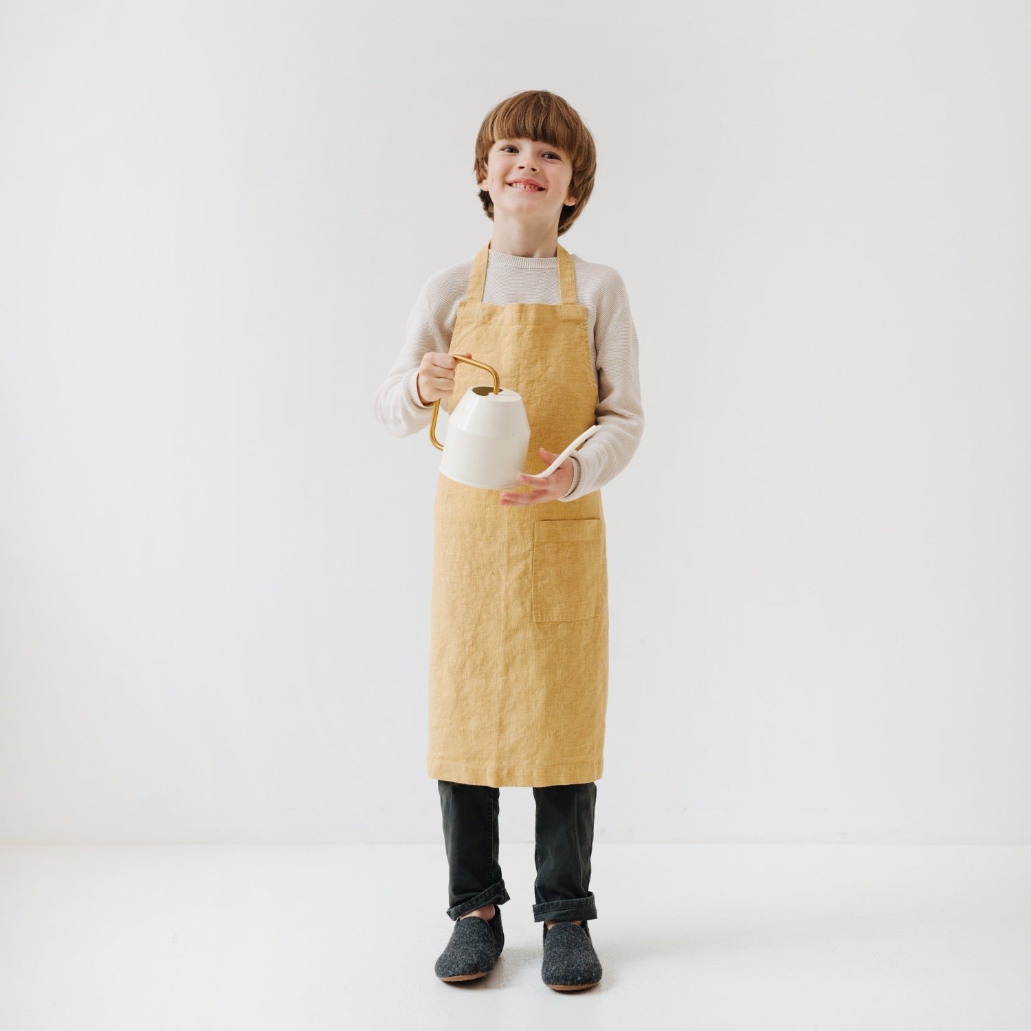 soft honey linen kids apron with a front pocket in warm morning light