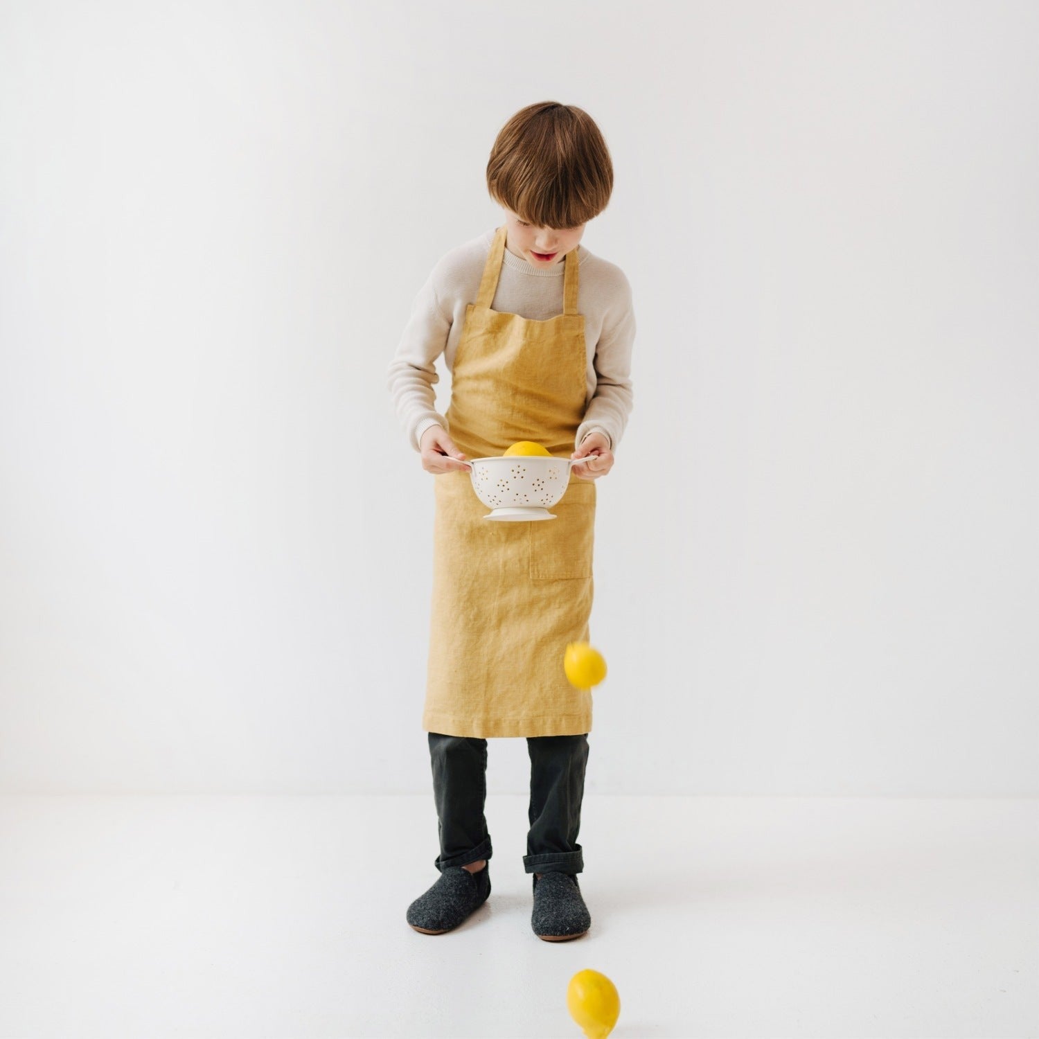 a playful child in a honey linen apron laughing while holding a wooden spoon