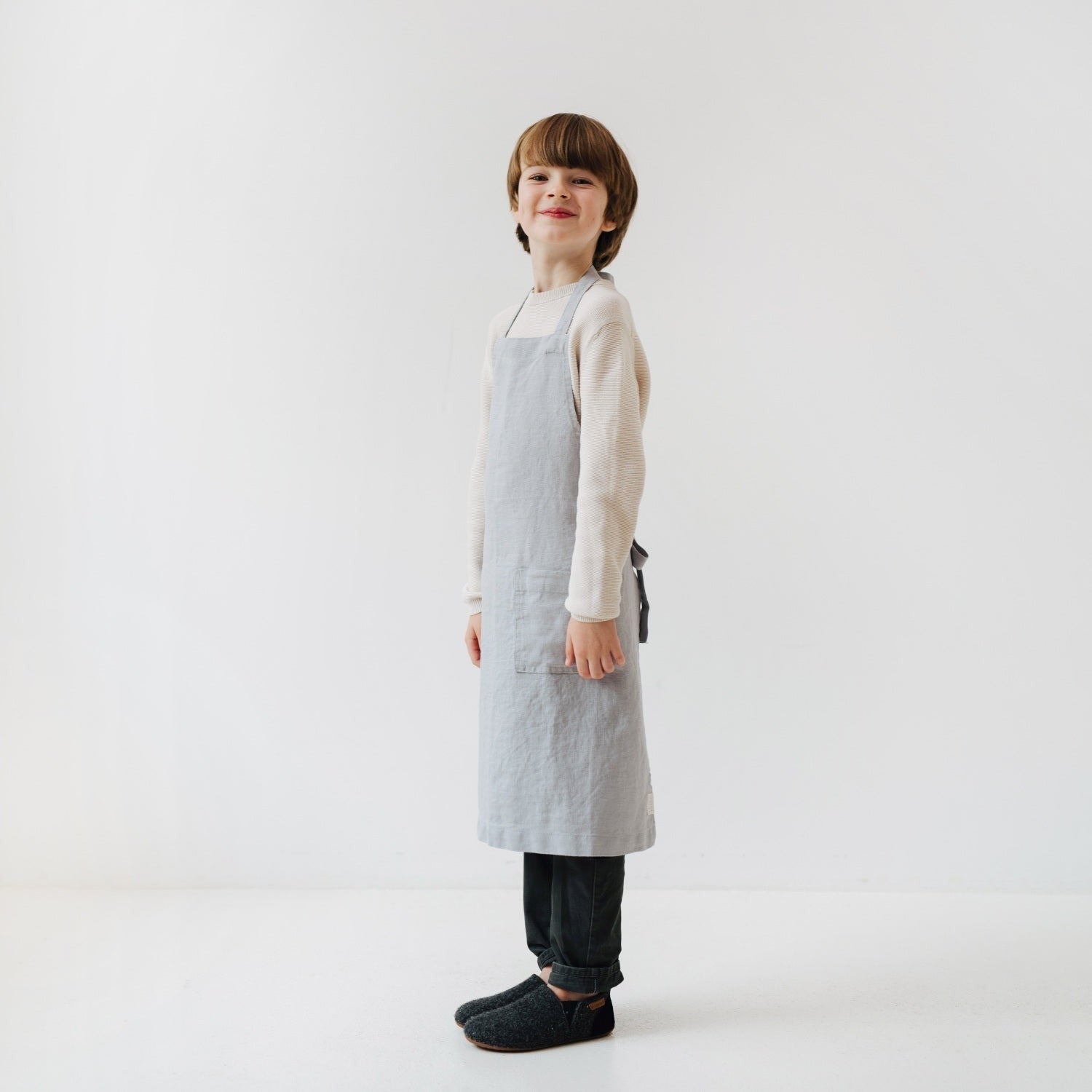 elegant light grey linen kids apron with a front pocket, shown in a refined kitchen setting
