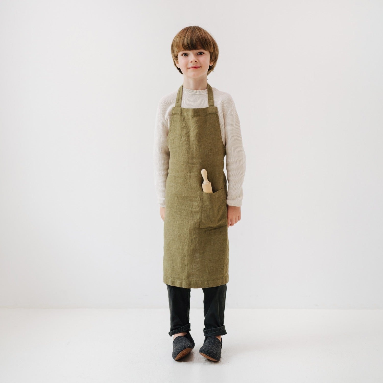close-up of a child's olive linen apron pocket holding a wooden spoon and measuring tape