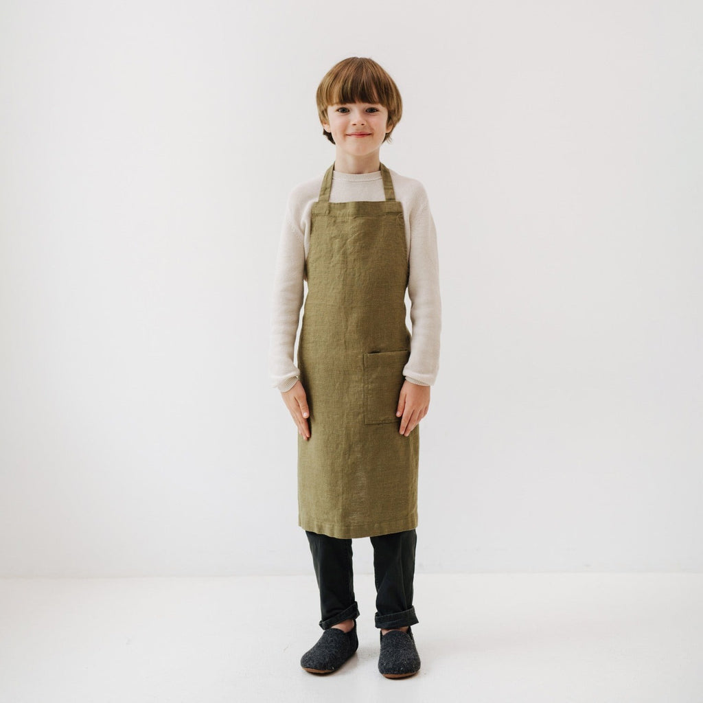 a young child in an olive linen apron laughing while playfully covered in flour